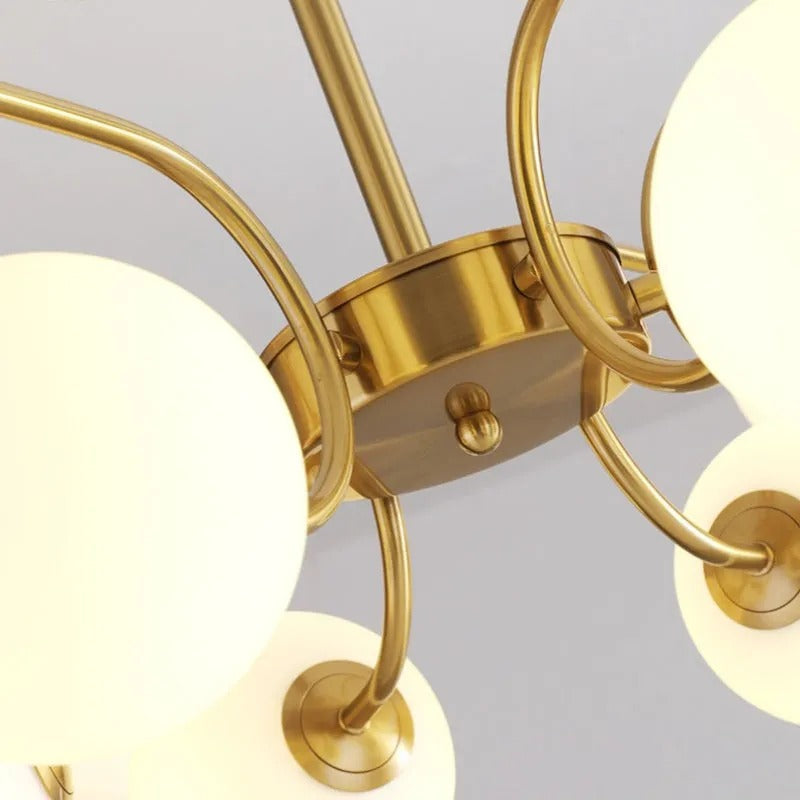 Close-up of the Clérachic chandelier's brass hub and ball finial, where the glass-globe arms meet the central mount.