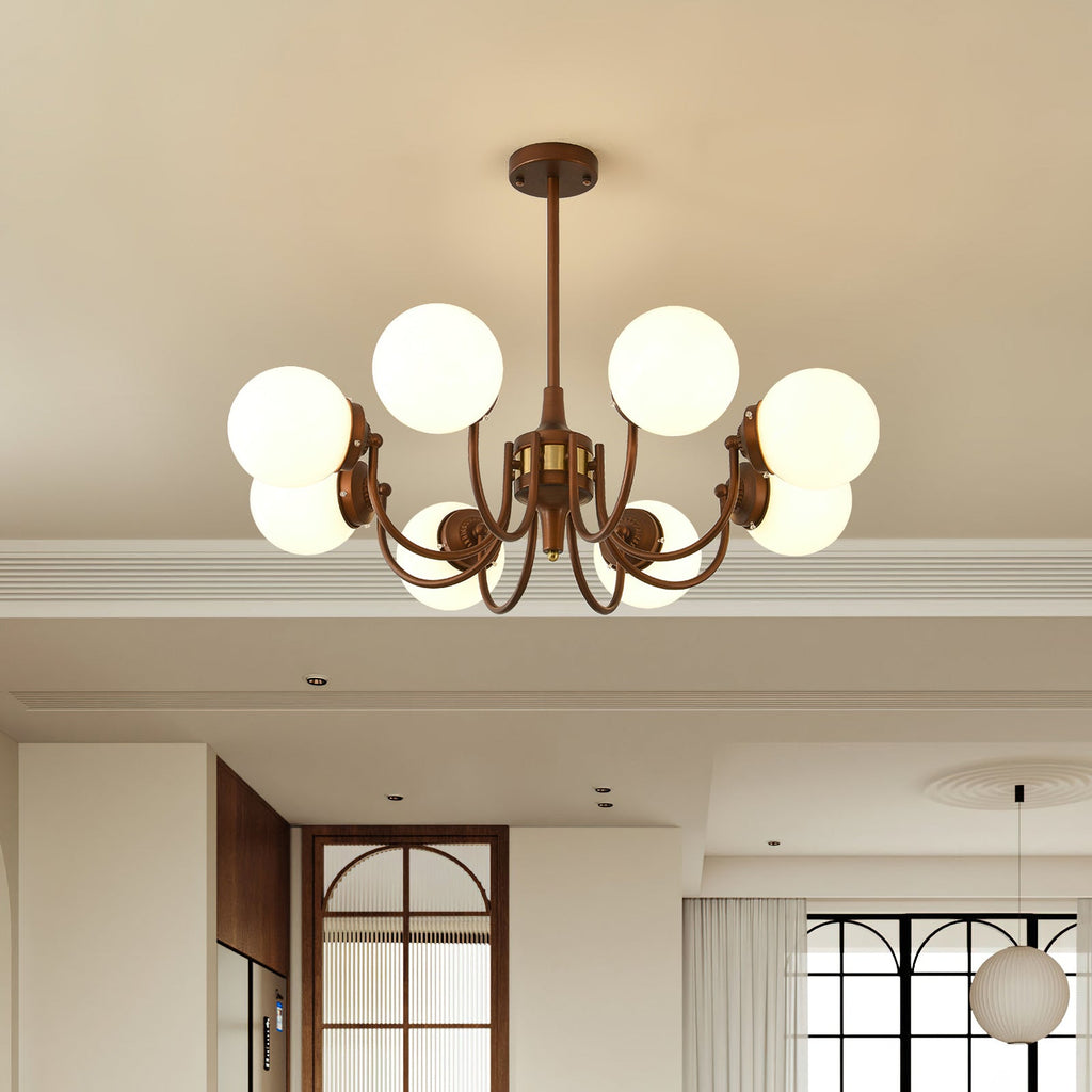 A lit Clérachic chandelier with eight white globes hangs in a cream room with an arched wooden door and a pendant beyond.