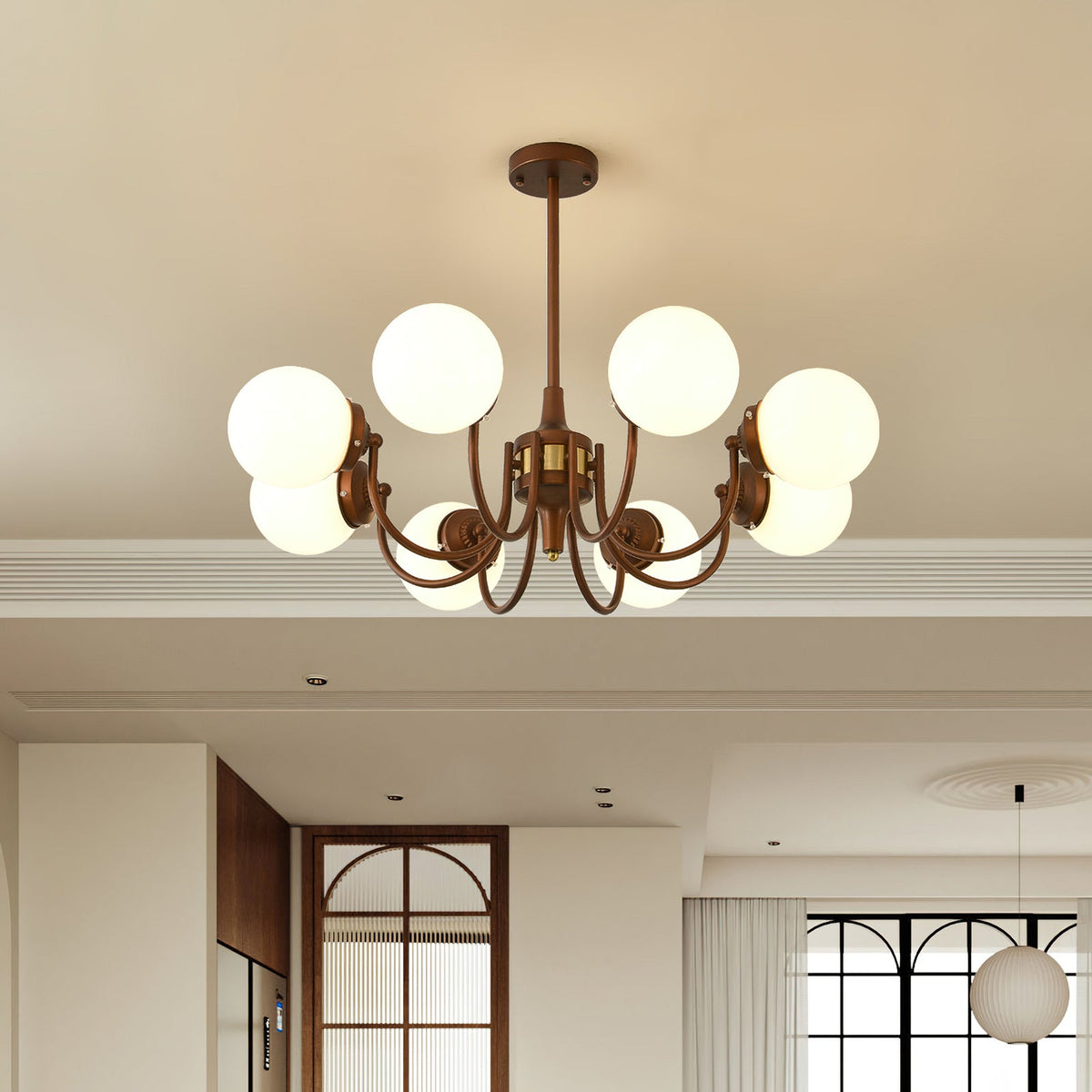 A lit Clérachic chandelier with eight white globes hangs in a cream room with an arched wooden door and a pendant beyond.