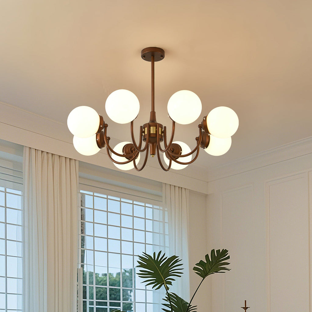 This Clérachic chandelier lights an airy room with white curtains and a gridded window, its globes spread on bronze curved arms.