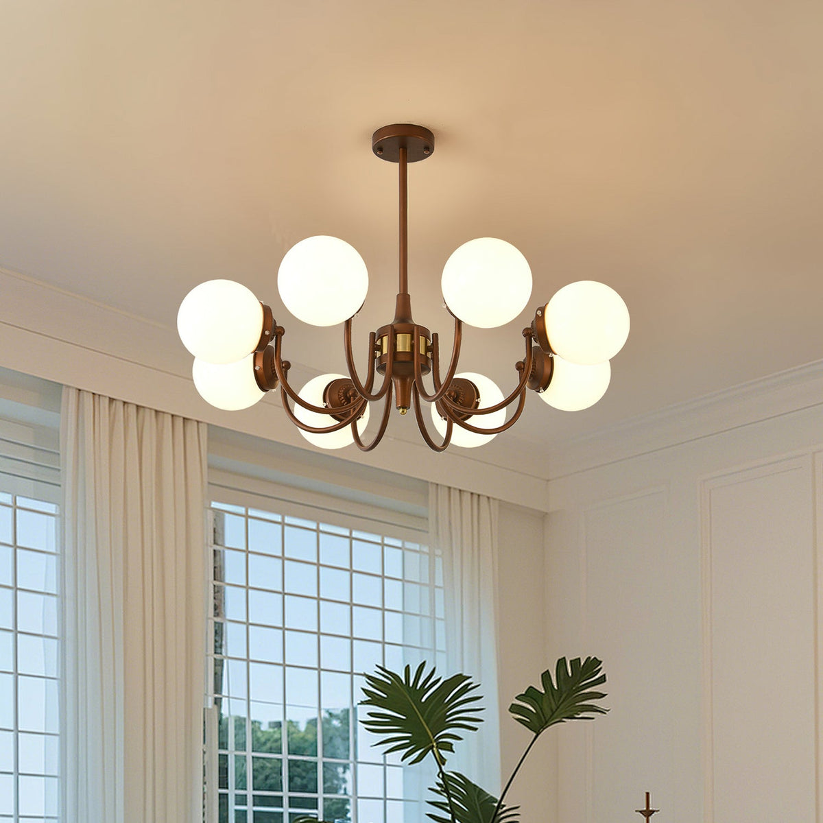 This Clérachic chandelier lights an airy room with white curtains and a gridded window, its globes spread on bronze curved arms.