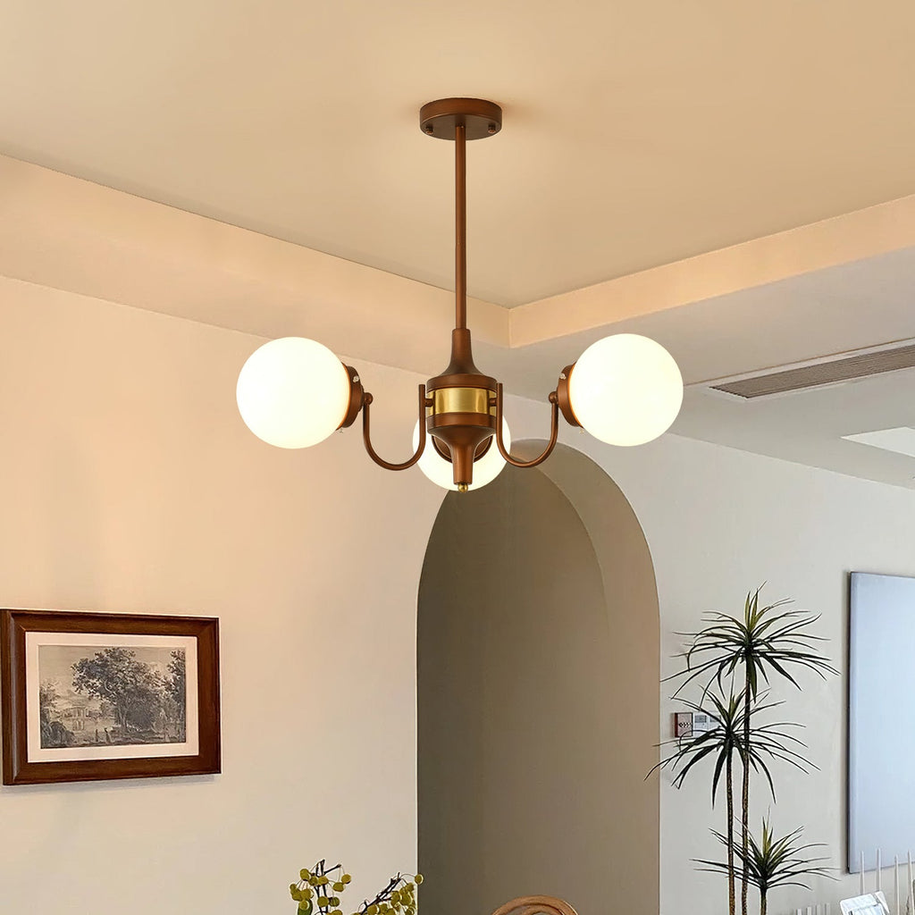 Three-globe Clérachic chandelier lit in a dining room with an arched doorway, a framed landscape print and a tall palm.