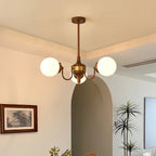 Three-globe Clérachic chandelier lit in a dining room with an arched doorway, a framed landscape print and a tall palm.