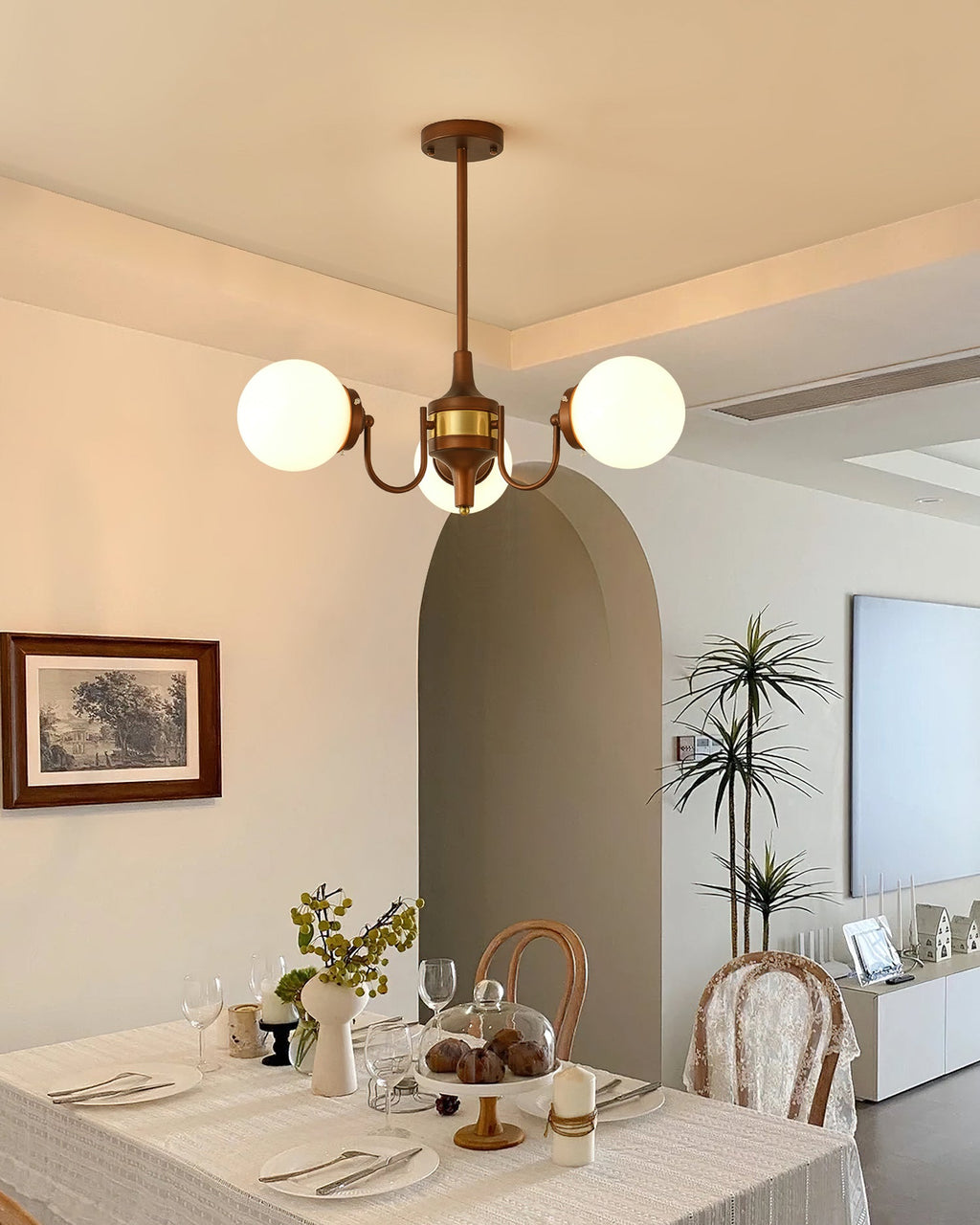 Three-light Clérachic chandelier above a laid dining table, with an arched doorway and a framed print on the wall.