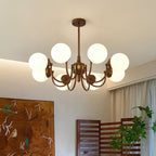 Looking up at an eight-light Clérachic chandelier with glowing white globes, beside a painted wooden screen and a leafy plant.