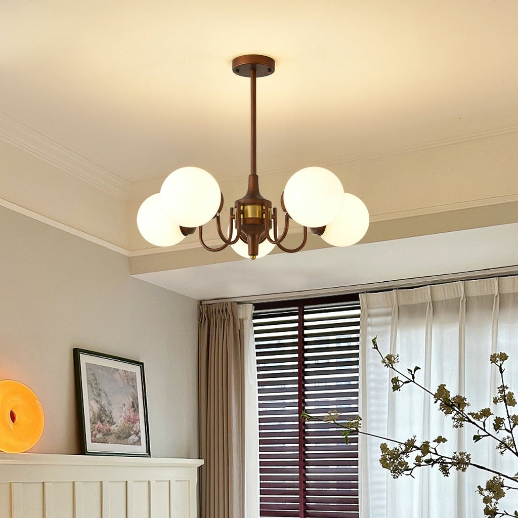 Smaller Clérachic chandelier with five white globes on bronze arms, lit in front of a window with sheer curtains.