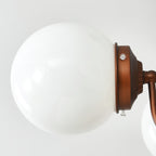 Close view of a white glass globe and its bronze holder with small screws on this Clérachic chandelier.