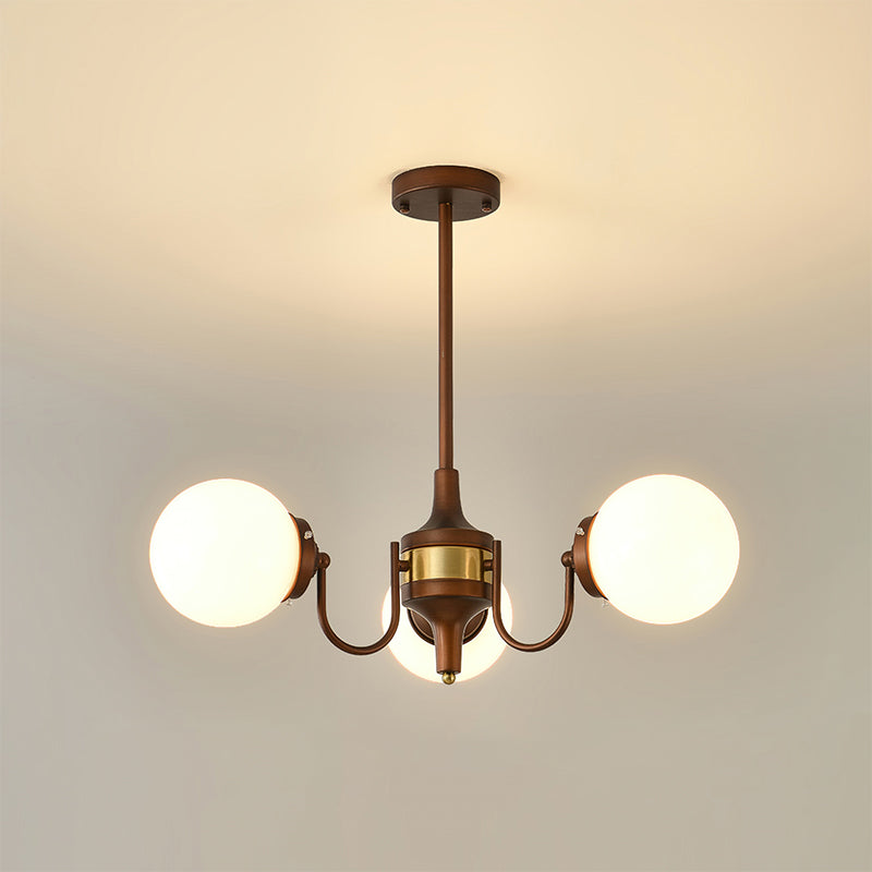 Three-light Clérachic chandelier lit with white globes on curved bronze arms and a brass band, hung from a short rod.