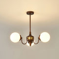 Three-light Clérachic chandelier lit with white globes on curved bronze arms and a brass band, hung from a short rod.