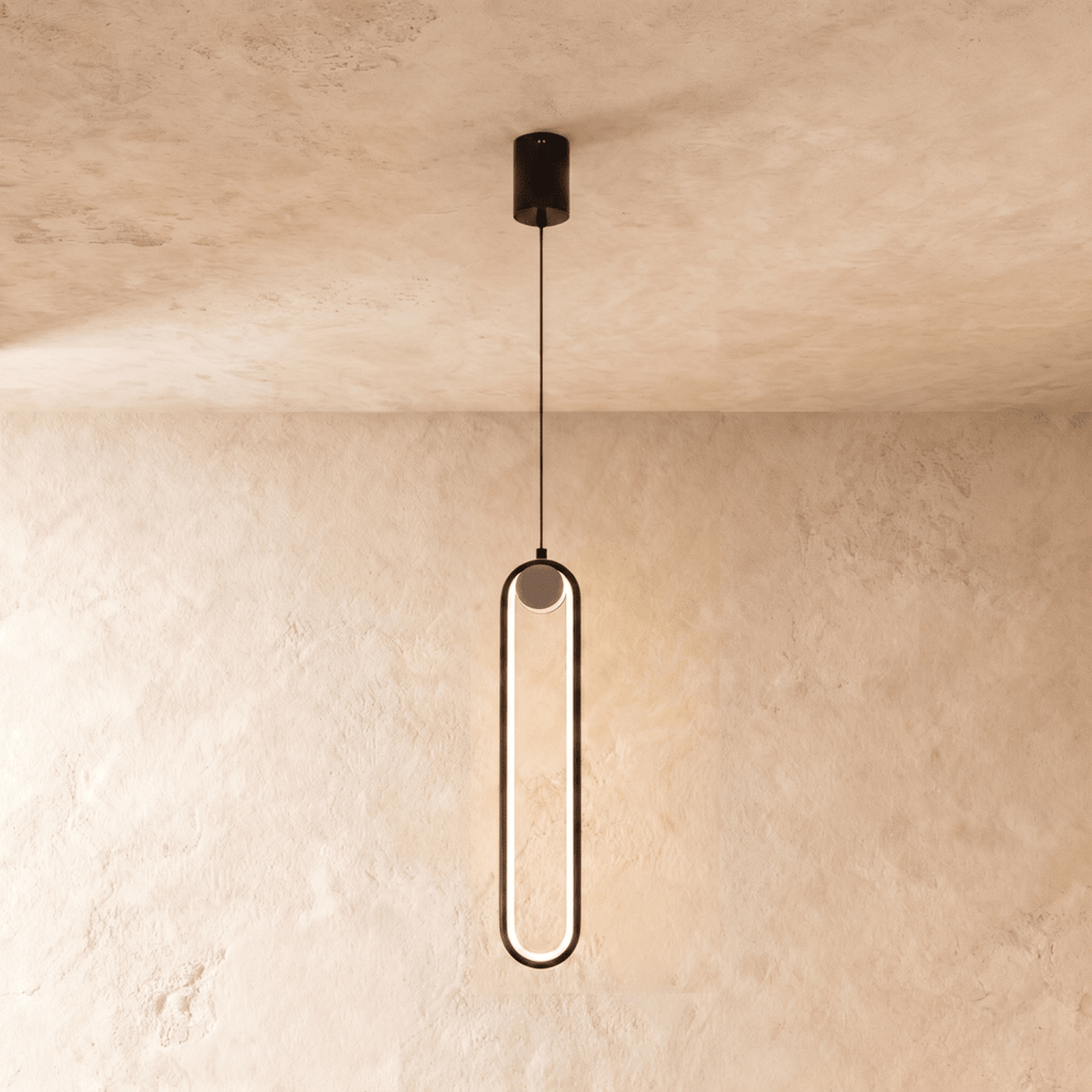 Clérachic slim black stadium-shaped LED pendant light with a small white globe at the top, glowing on a limewash wall.