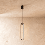 Clérachic slim black stadium-shaped LED pendant light with a small white globe at the top, glowing on a limewash wall.