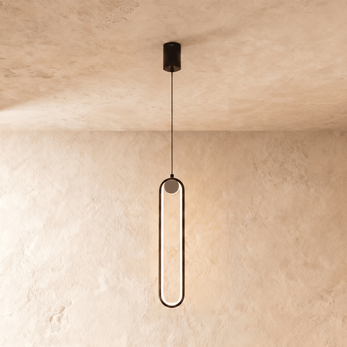 Clérachic slim black stadium-shaped LED pendant light with a small white globe at the top, glowing on a limewash wall.