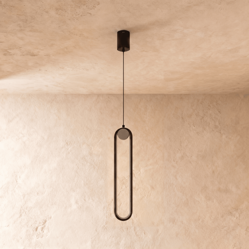 Clérachic slim black stadium-shaped pendant light with a small white globe, switched off, on a limewash wall.