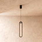 Clérachic slim black stadium-shaped pendant light with a small white globe, switched off, on a limewash wall.