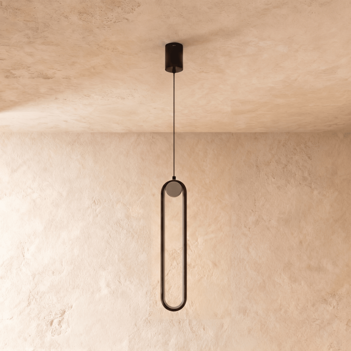 Clérachic slim black stadium-shaped pendant light with a small white globe, switched off, on a limewash wall.