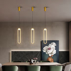 Clérachic row of three gold stadium-shaped LED pendant lights hung above a long dining table with green chairs.