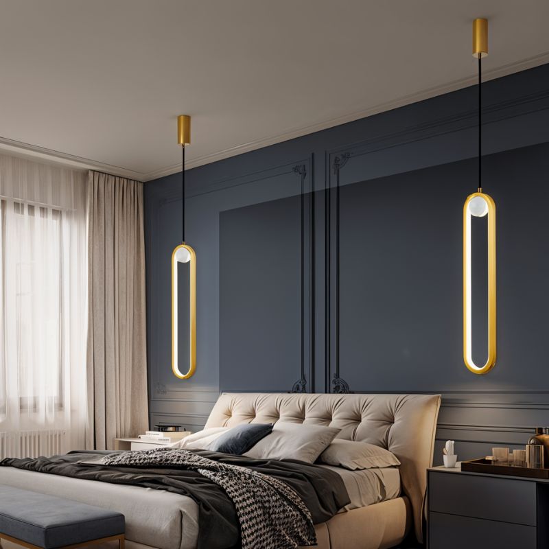 Clérachic pair of gold stadium-shaped LED pendants hung at different heights beside a bed against a navy panelled wall.