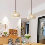 Two Clérachic woven pendants at different heights above a wooden dining area, with white flowers and a sideboard with glazed doors.