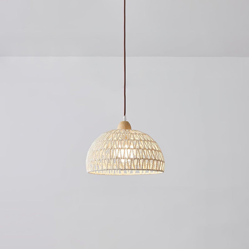 Smaller Clérachic dome pendant hanging in a plain grey room, the open weave showing a soft light inside and a brown cord above.