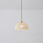 Smaller Clérachic dome pendant hanging in a plain grey room, the open weave showing a soft light inside and a brown cord above.