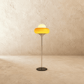 Clérachic floor lamp in yellow glass, its rounded shade glowing atop a slim chrome stem and round black metal base.