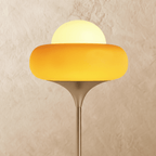 A close view of the Clérachic floor lamp's yellow glass shade, its white globe glowing warmly against a plaster wall.