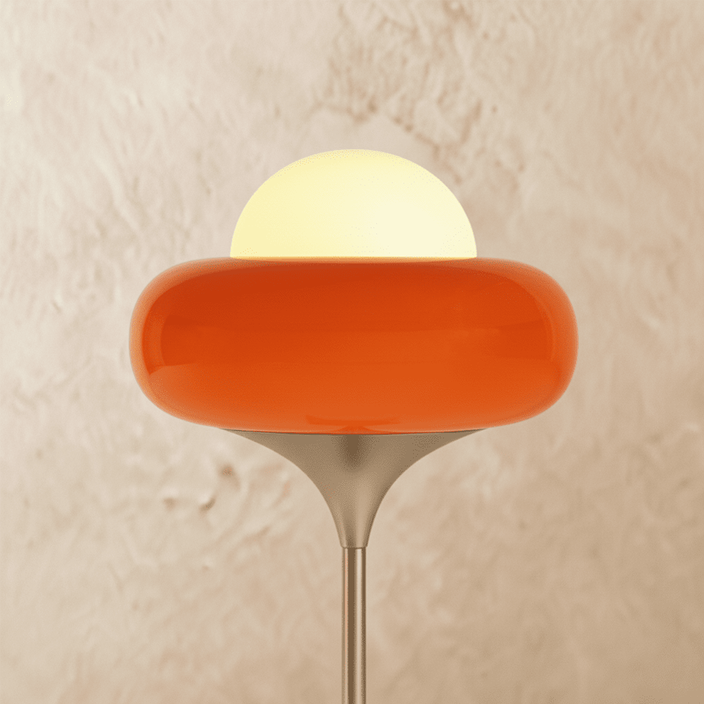 A close view of the Clérachic floor lamp's orange glass shade, its white globe glowing warmly against a plaster wall.
