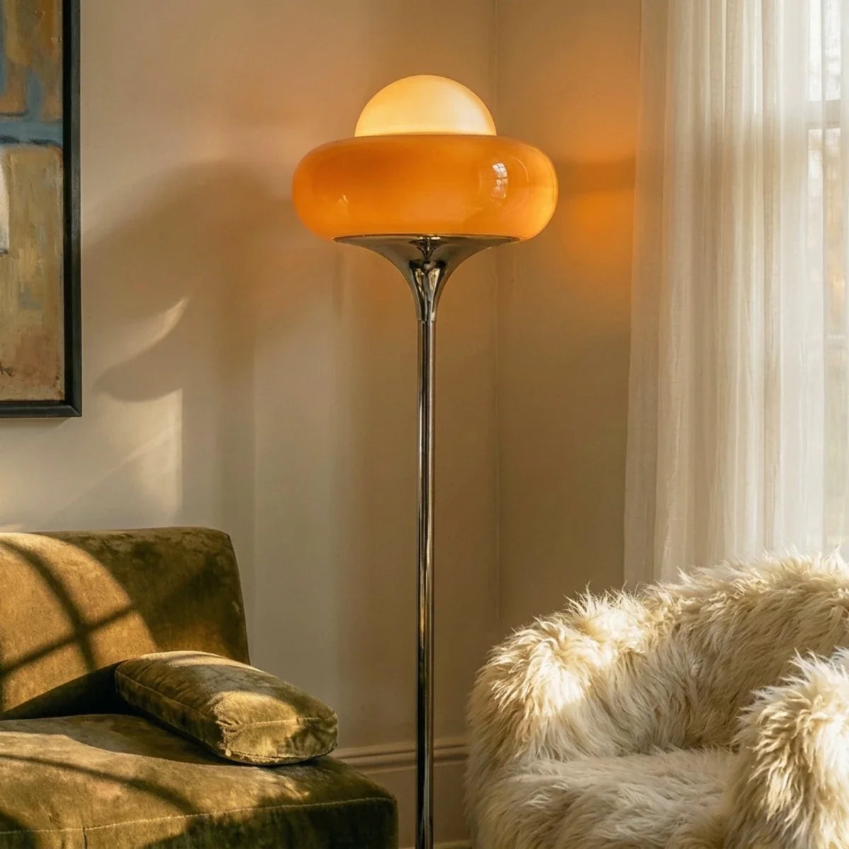 Close-up of the Clérachic floor lamp's orange glass shade glowing beside an olive velvet sofa and sheer curtains.