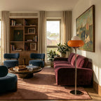 A Clérachic floor lamp in orange glass stands beside a burgundy sofa under a framed painting.