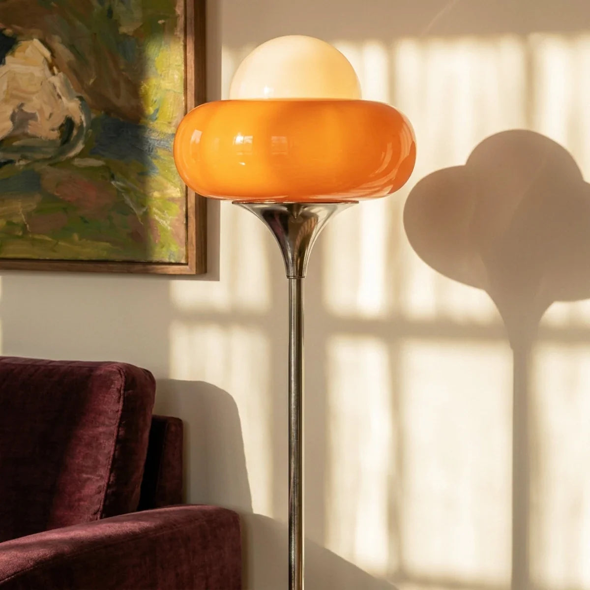 Close-up of the Clérachic floor lamp's orange glass shade lit warmly against a painted wall.