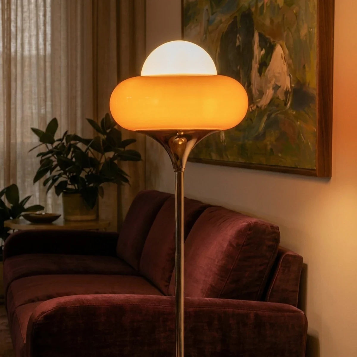 An evening close-up of the Clérachic floor lamp's orange glass shade beside a velvet sofa.