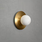 Clérachic Orb sconce on a grey wall, brushed brass disc set behind a round alabaster globe.
