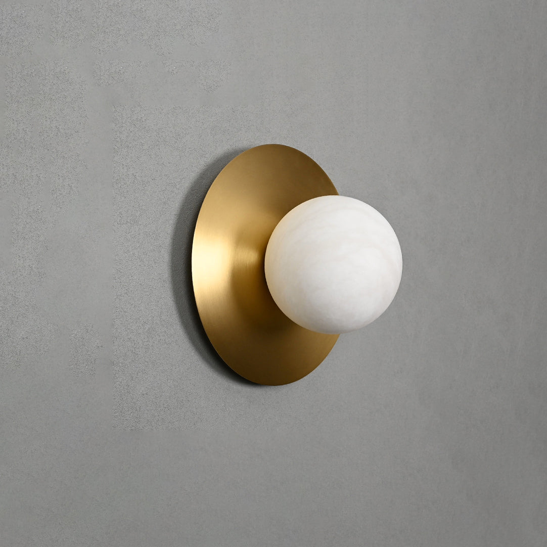 Clérachic Orb sconce on a grey wall, brushed brass disc set behind a round alabaster globe.