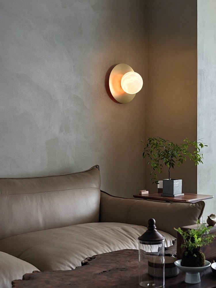 Clérachic Orb sconce lit in a plaster corner above a leather sofa and small side table.