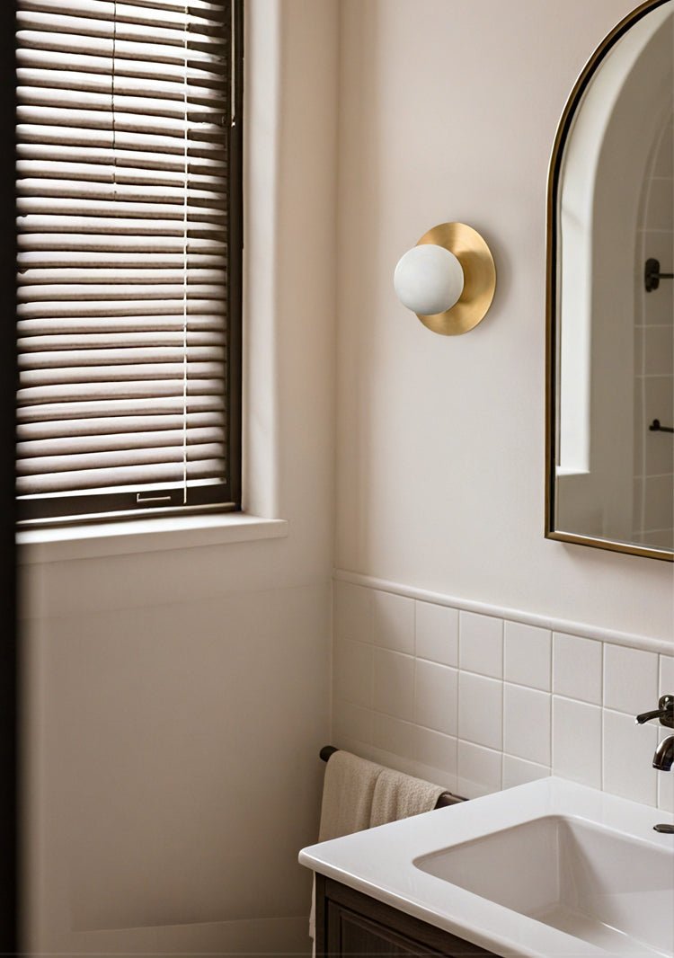 Clérachic Orb sconce beside an arched mirror in a bathroom, daylight through timber blinds.