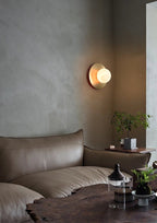 Clérachic Orb wall sconce lit close on grey plaster, warm light rimming the brass backplate.