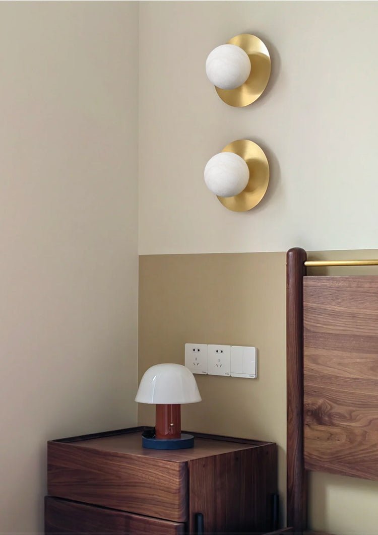 A pair of Clérachic Orb sconces stacked above a walnut nightstand and small mushroom lamp.
