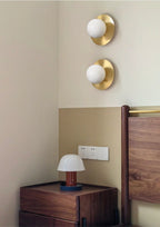 A pair of Clérachic Orb sconces stacked above a walnut nightstand and small mushroom lamp.