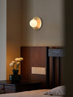 The Clérachic Orb sconce casting warm light down a bedroom wall onto a wooden bed frame.
