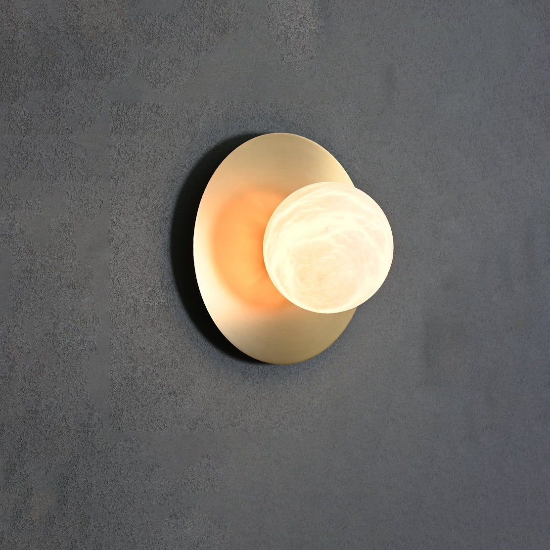 Clérachic Orb sconce glowing against dark grey concrete, alabaster globe softly translucent.