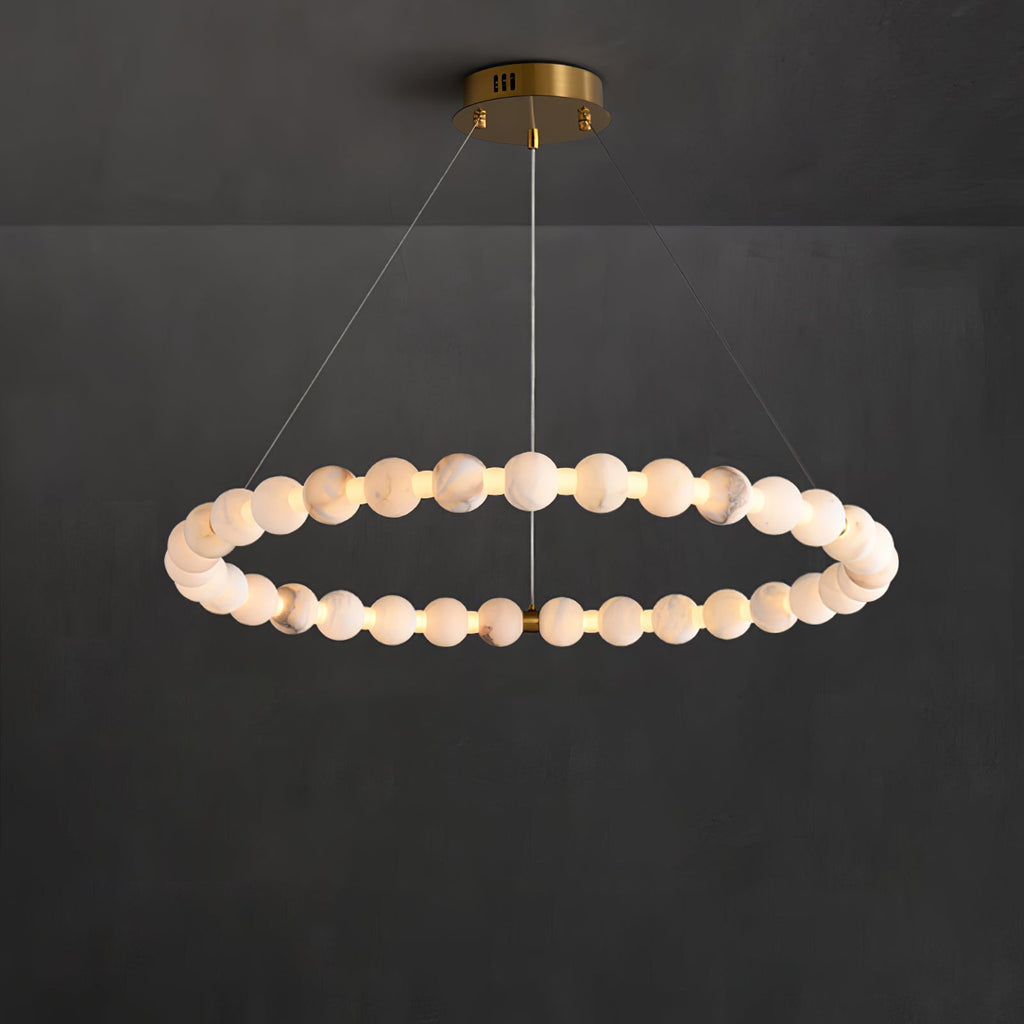 The Clérachic Orb ring chandelier lit against dark plaster, beads glowing evenly around it.