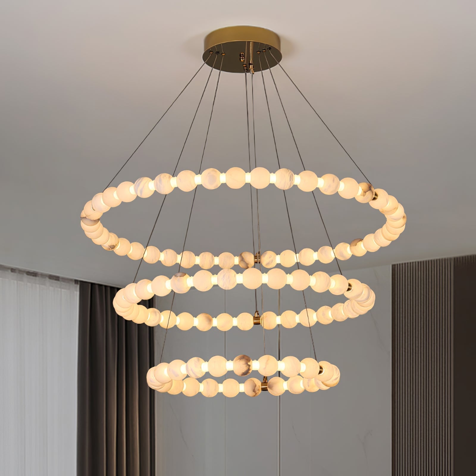 Clérachic Orb chandelier in three tiers, hung beside floor-length curtains in a pale room.