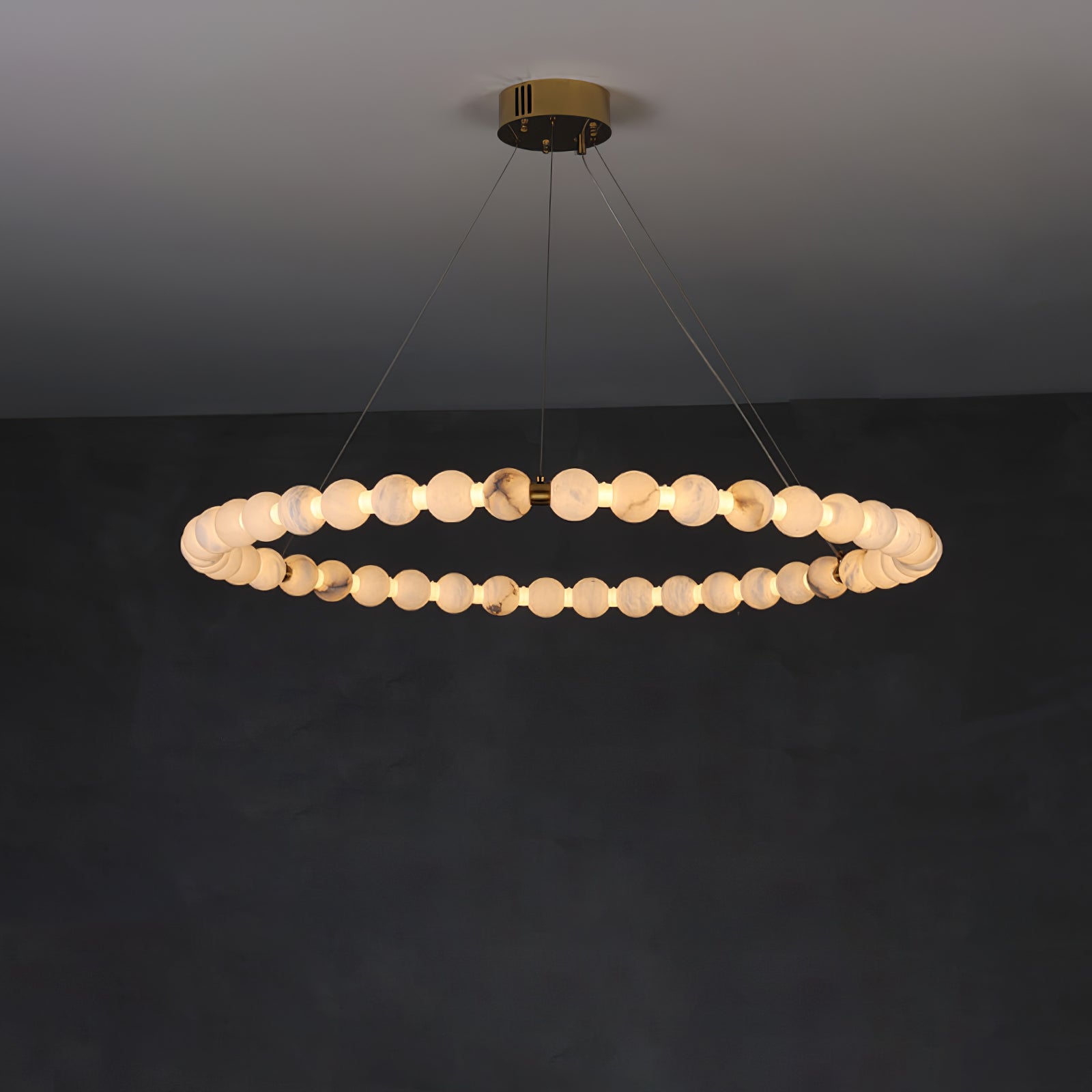 Clérachic Orb ring chandelier lit wide on a dark wall, brass canopy flush to the ceiling.