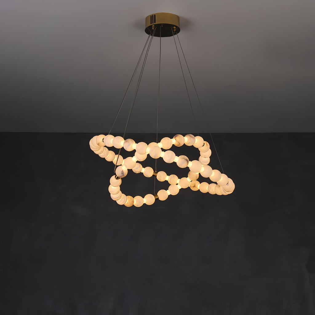 The Clérachic Orb chandelier looping in on itself, alabaster beads lit warm on charcoal.