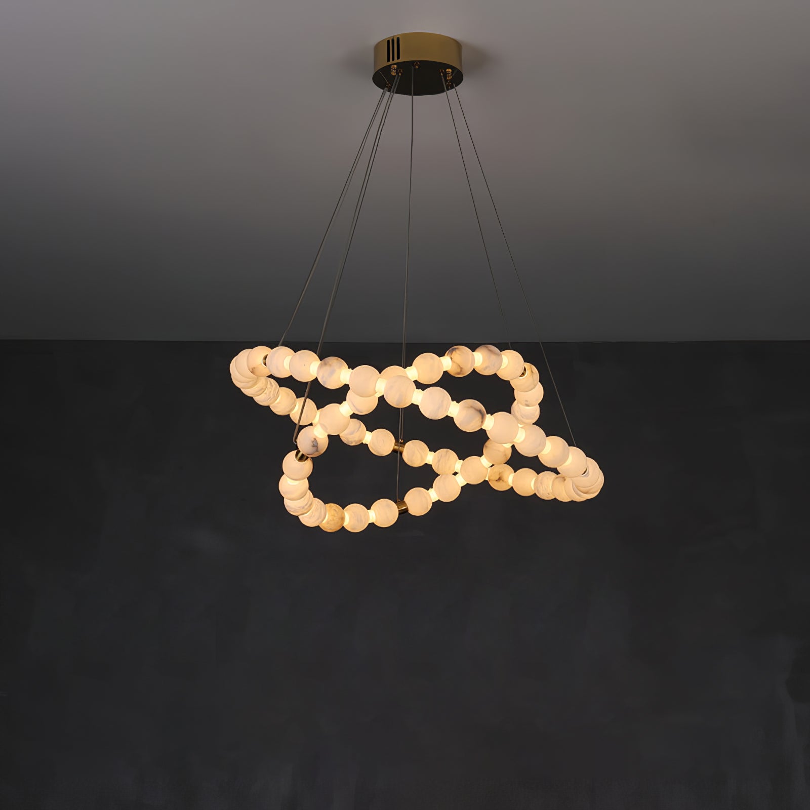 The Clérachic Orb chandelier looping in on itself, alabaster beads lit warm on charcoal.