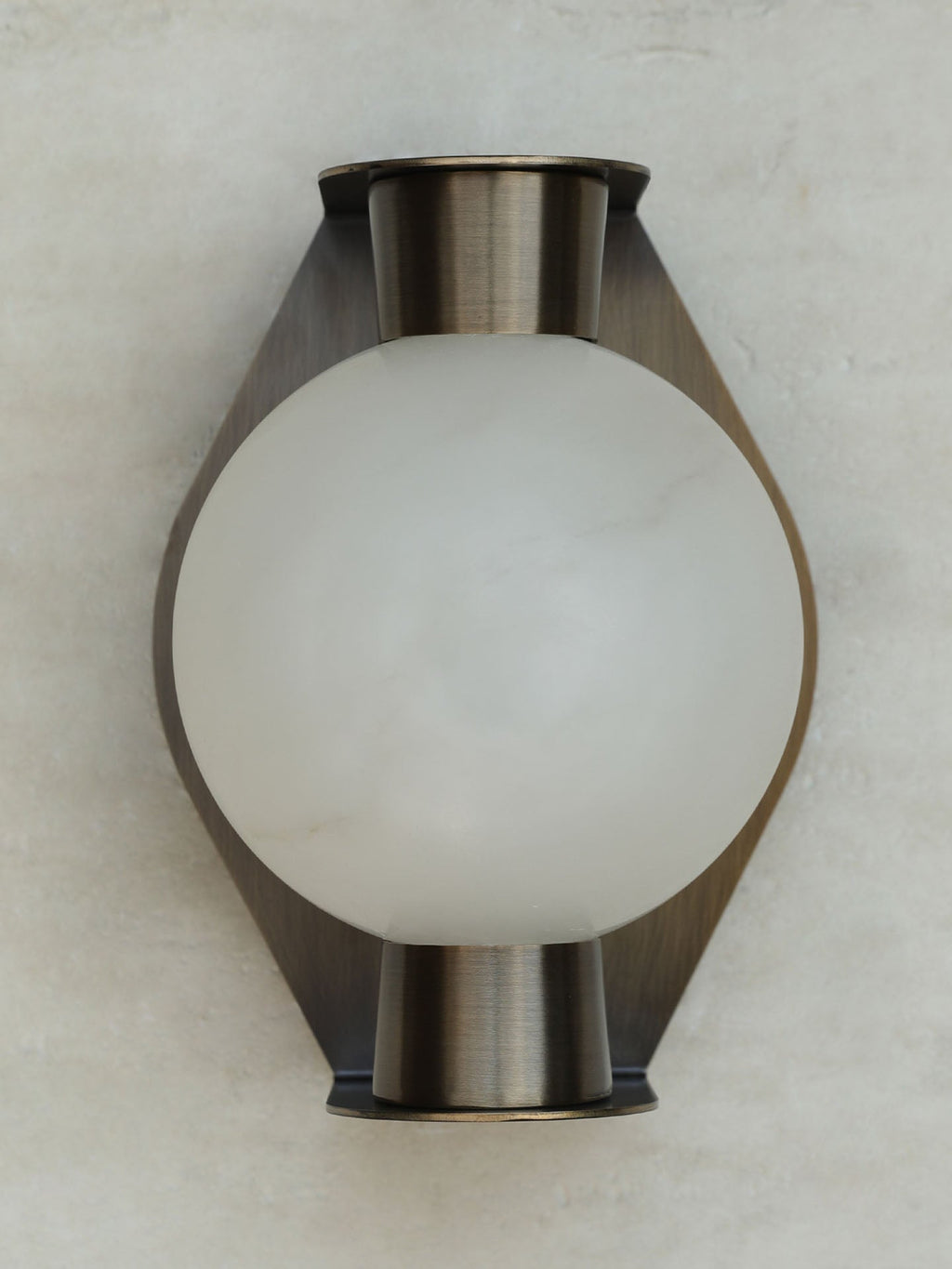 The Clérachic Orb sconce unlit on grey, brushed bronze plate curving behind the stone globe.