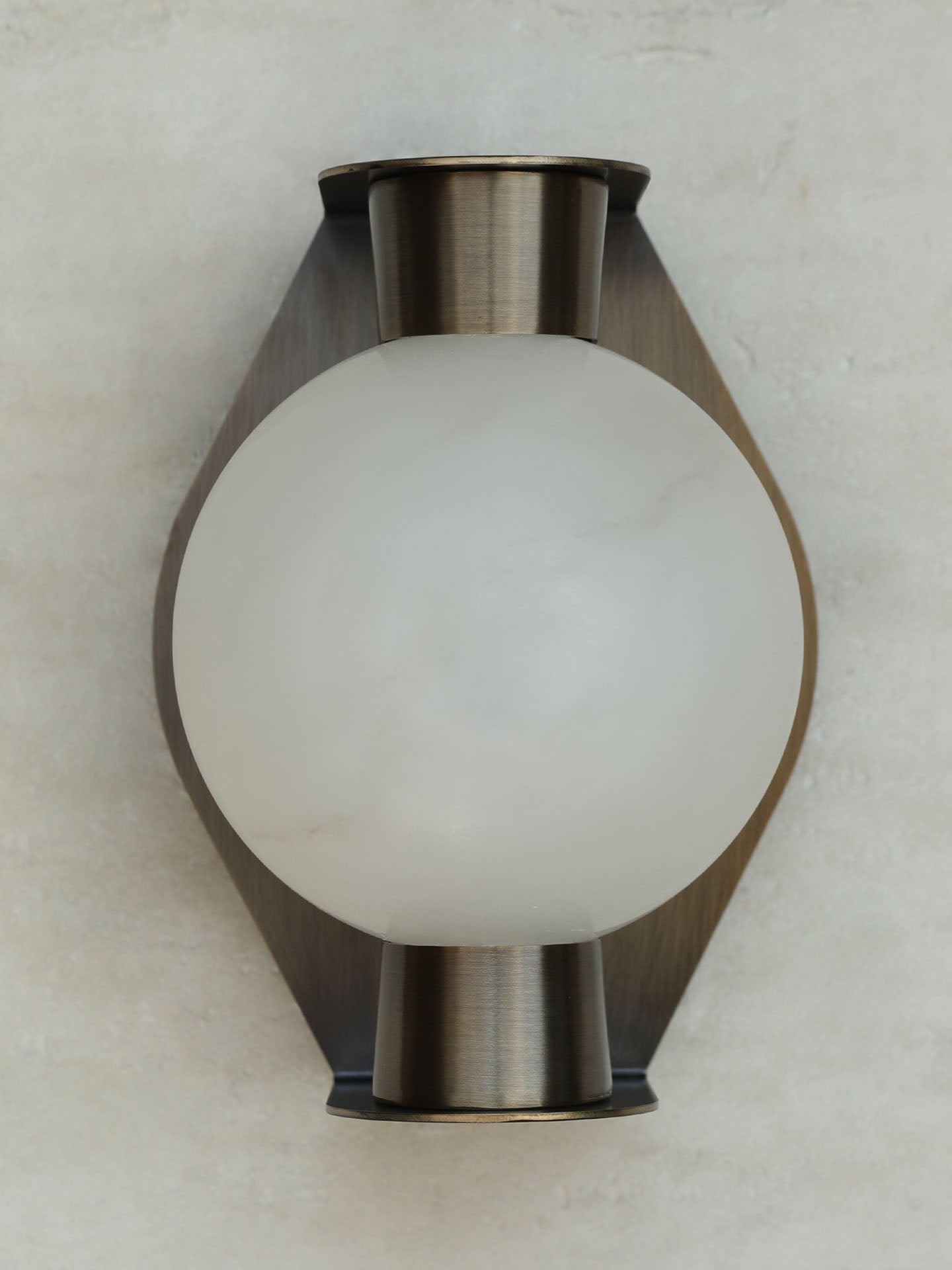 The Clérachic Orb sconce unlit on grey, brushed bronze plate curving behind the stone globe.