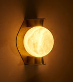Clérachic Orb sconce lit on an ochre wall, warm light spilling around the alabaster sphere.