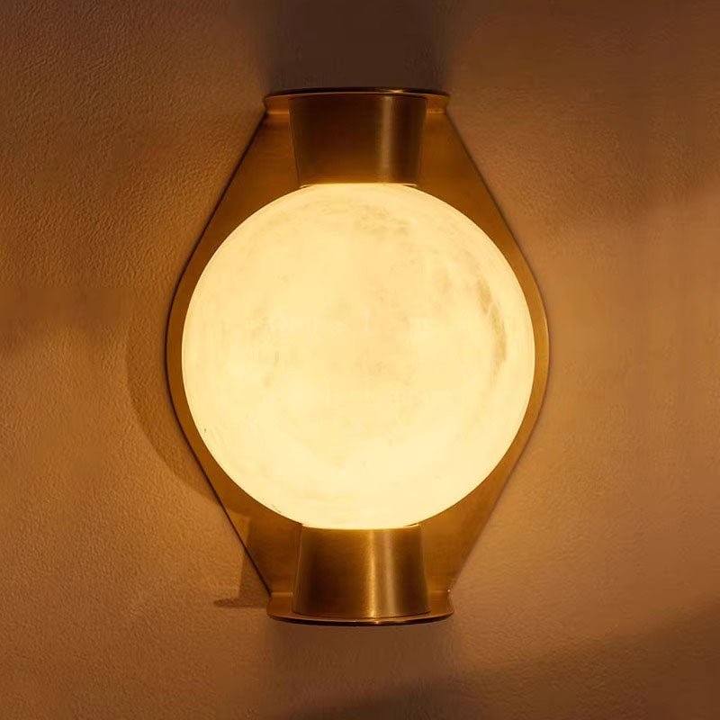 Clérachic Orb sconce in brass finish, glowing globe centred on the tapered backplate.