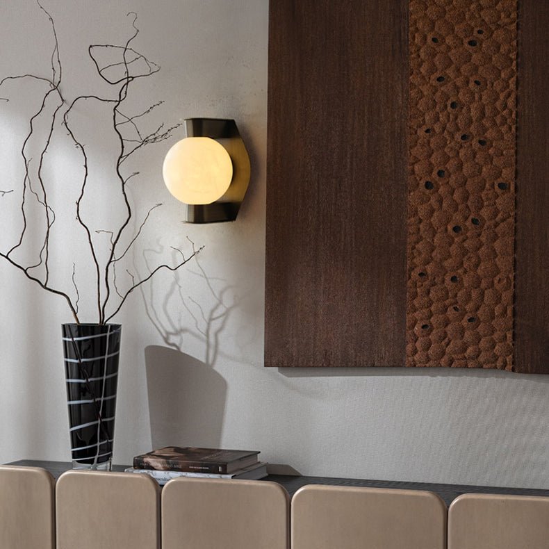 The Clérachic Orb sconce beside a dark timber panel and a vase of bare branches.